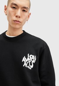 Sort sweatshirt lavet af bomuld med rund hals, der har et hvidt forvrænget logo på brystet. Glat tekstur og afslappet pasform.