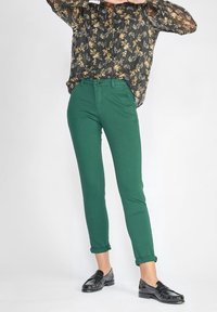 Gröna bomullshängselbyxor med slim fit, avsmalnande ben och uppvikta fållar. Bärs med en svart blommig blus och svarta loafers.