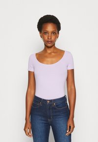 Svetlo vijolična bodysuit s kratkimi rokavi in okroglo ovratnikom, v kombinaciji s temno modrimi skinny kavbojkami. Material izgleda gladek in raztegljiv.