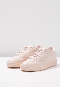 Jasnoróżowe skórzane sneakersy o niskim profilu, zaokrąglonym nosku, z perforowanymi akcentami i płaskimi sznurowadłami. Teksturowana gumowa podeszwa zapewniająca przyczepność.