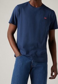 Navyblaues Baumwoll-T-Shirt mit kurzen Ärmeln, rundem Ausschnitt und kleinem roten Levi's-Logo auf der Brust. Getragen mit hellblauen Jeans.