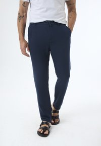 Navy blue pants in a lightweight fabric, featuring a slim fit, side pockets, and a drawstring waist. Matched with black strappy sandals.
