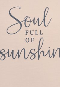 Ljust rosa tyg med mörkblå text som säger "Själ FULL AV solsken." Slät textur, enkel design som betonar texten.