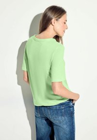 Ljusgrön t-shirt med kort ärm och rund halsringning, ihopparad med blå denimjeans. T-shirten har en avslappnad passform och len textur.