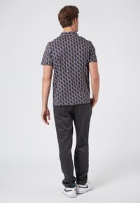 Camisa de manga corta con un patrón geométrico que presenta colores azul, rojo y beige, combinada con pantalones gris oscuro y zapatillas blancas.