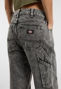 Pantalones cargo de mezclilla gris con una textura deslavada, que cuentan con múltiples bolsillos y un parche de logo en el bolsillo trasero. Corte de talle alto ajustado.
