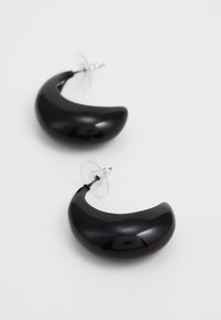 Svarte akryl halvmåneformede øreringer med blank finish og klare bakker for sikker bæring. Lett og buet design.