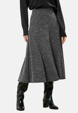 Donna che indossa una gonna midi grigia a vita alta con trama, abbinata a stivali neri lucidi alti fino al ginocchio con tacco e un maglione nero.