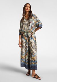 Tulostettu haalari monivärisillä kuvioilla, väljällä istuvuudella, lyhyillä hihoilla ja nauhavyötäröllä. Yhdistetty ruskeisiin sandaaleihin.