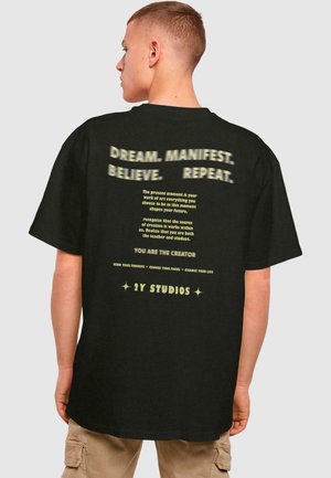 Sort oversized t-shirt med fed gul tekst på ryggen, der indeholder motiverende sætninger og et brandnavn nederst.