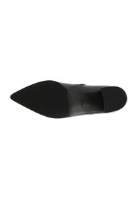 Chaussure noire à bout pointu avec une tige en cuir lisse et une texture subtile. Dotée d'une semelle en caoutchouc plate avec des rainures horizontales pour l'adhérence.