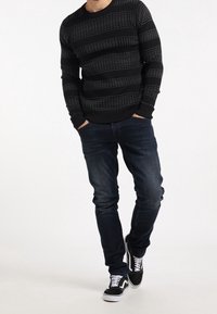 Maglione nero a maglia con strisce grigie orizzontali, abbinato a jeans slim-fit blu scuro e sneakers bianco e nere.