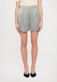 Shorts gris ajustés avec des plis, longueur mi-thigh, fabriqués en tissu lisse. Portés avec un haut léger et des ballerines noires à bout pointu.