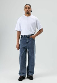 Witte T-shirt met korte mouwen en losse, medium blauwe spijkerbroek. Draag je met zwarte plateau schoenen met dikke zolen en rode veters.