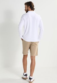 White long-sleeve polo shirt, beige shorts, and white sneakers with black and red accents, viewed from the back against a light background.