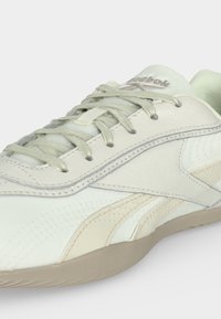 Ανοιχτό μπεζ και ανοιχτό λευκό παπούτσι Reebok με κορδόνια, κεντημένες λεπτομέρειες λογότυπου και επίπεδη λαστιχένια σόλα.