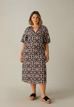 Bedrucktes Baumwoll-Maxikleid mit V-Ausschnitt und kurzen Ärmeln, das ein geometrisches Muster in Marine- und Beigetönen aufweist. Getragen mit schwarzen Plateausandalen.