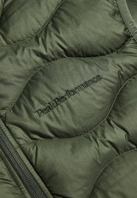 Maslinasto zeleni bundić s quilted ispravom, sa glatkom završnom obradom, s izvezenim "PeakPerformance" logotipom i detaljima na rasklopu.