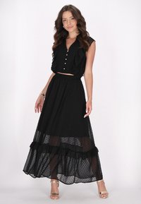 Schwarzes Punktmuster-Zweiteiler-Set mit einem kurzen Top mit Rüschen und Knopfdetails, kombiniert mit einem schwingenden, gestuften Maxikleid.
