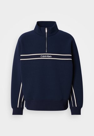 Navy blue sweatshirt with a half-zip collar, white stripes across the chest, and branding at the center. Knit texture with ribbed cuffs.