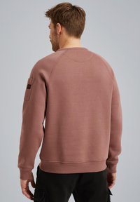 Sudadera marrón con cuello redondo, puños y dobladillo acanalados, tela texturizada y un bolsillo de parche en la manga izquierda.