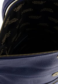 Niebieskie skórzane wnętrze torby z złotym zamkiem i materiałowym wykończeniem z powtarzającym się logo "VENEZIA" w złotym kolorze na czarnym tle.