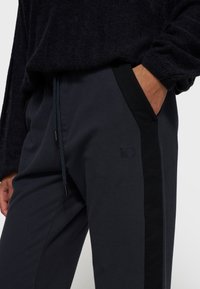 Marine joggers met zwarte zijstrepen, elastische tailleband met trekkoord, en tonale geborduurde nummer "10" bij de zak. Zachte stoftextuur.