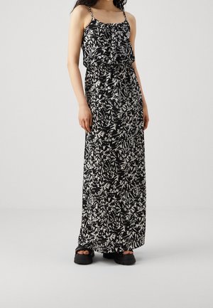 Robe longue à fines bretelles ; motif floral noir et blanc ; corsage à volants ; silhouette fluide ; tissu texturé ; associée à des sandales noires épaisses.