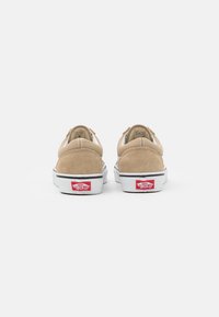 Sneaker basse in suede beige con suole in gomma bianca e dettaglio del logo rosso sul tallone. Presentano un colletto imbottito e un design minimalista.