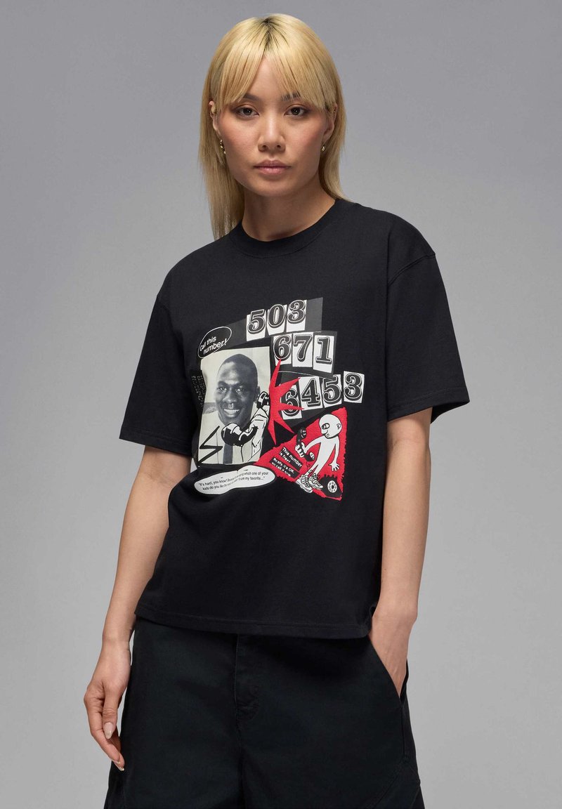 Camiseta de algodón negra con un estampado gráfico que incluye texto, imágenes y colores llamativos, con acentos rojos y una ilustración estilo cómic.