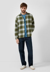 Flanelowa koszula w zielono-białą kratę nałożona na niebieski T-shirt, zestawiona z ciemnymi dżinsami i białymi tenisówkami. Prosty, casualowy styl.