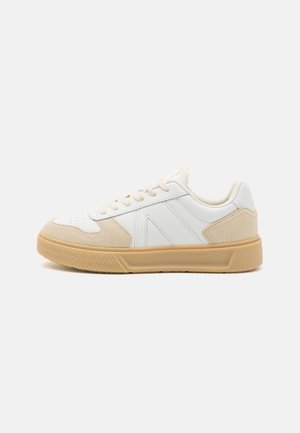 Weißer Low-Top-Sneaker mit beigen Wildlederakzenten und Gummisohle, seitlich auf schlichtem Hintergrund gezeigt.