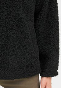 Black fleece pullover, textured with a soft, shaggy exterior, featuring a relaxed fit and no visible hardware or patterns.