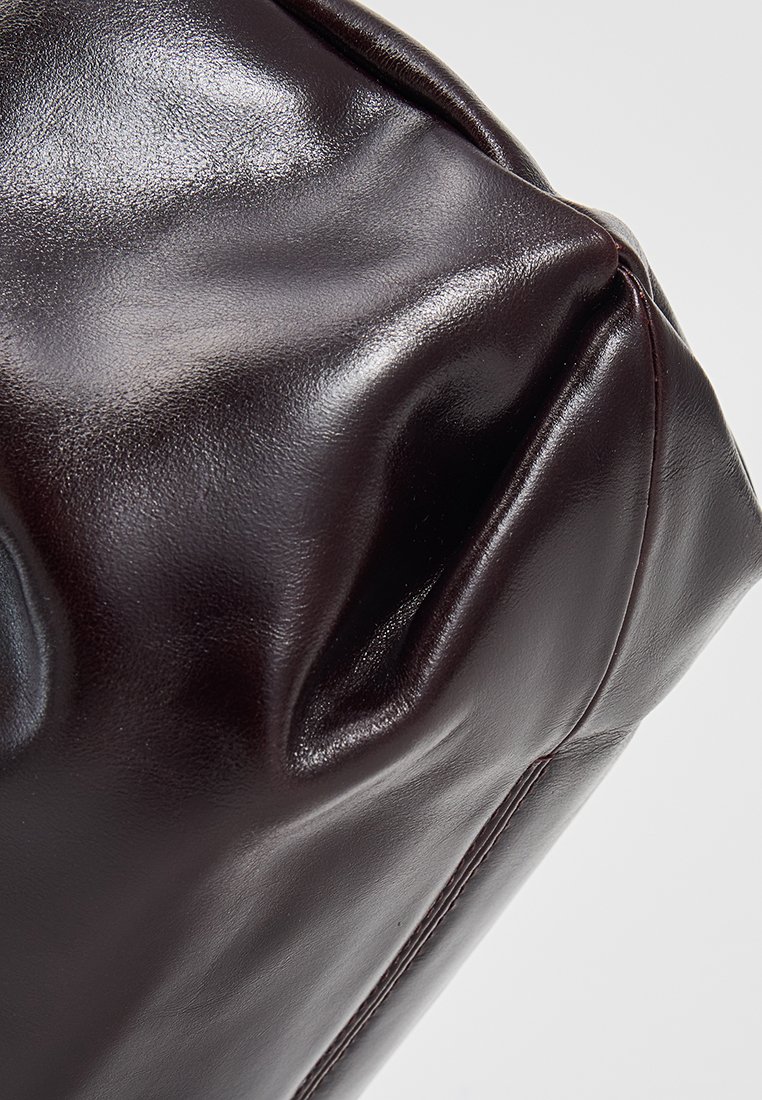 Sac en cuir bourgogne foncé avec une texture lisse et brillante, mettant en avant de douces plis et des détails de couture subtils. Forme arrondie et structurée.