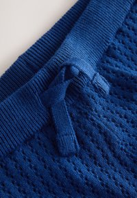 Tessuto lavorato a maglia blu con vita a coste e coulisse annodata, caratterizzato da un motivo testurizzato e traspirante.