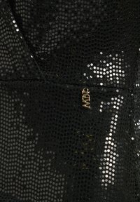Tissu noir à paillettes avec un motif texturé, mettant en avant un accent en métal doré près du bord inférieur.