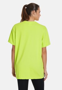 Neon grön t-shirt med kort ärm och lös passform. Mjuk tyg, rund hals och nederkanten faller under midjan. Inga synliga mönster eller detaljer.