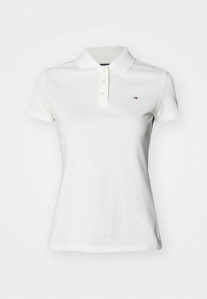 Λευκό πόλο μπλουζάκι φτιαγμένο από βαμβάκι, με γιακά και κλείσιμο με τρία κουμπιά. Περιλαμβάνει ένα μικρό λογότυπο στο στήθος. Κοντά μανίκια.