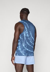 Débardeur bleu tie-dye avec un col rond et un motif texturé, associé à un short perforé bleu clair. Il présente une coupe décontractée.