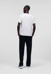 Tricou alb cu mânecă scurtă, pantaloni negri cu croială lejeră și adidași albi. Material neted, design minimalist, cu o textură ușoară pe adidași.