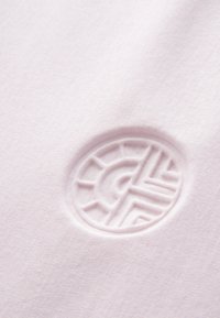 Tessuto rosa chiaro con una texture liscia presenta un logo circolare in rilievo al centro, che mostra motivi geometrici e dettagli.
