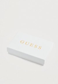 Scatola rettangolare bianca con finitura testurizzata, con la parola "GUESS" in lettere dorate sul coperchio.