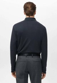 Temno modra polo majica z dolgimi rokavi in mehko teksturo, kombinirana s sivimi krojenimi hlačami z gladkim zaključkom in pasom.