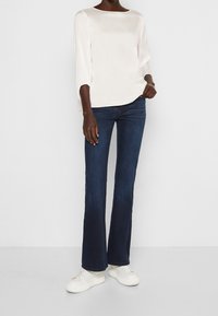 Cremfarbene Sat blouse mit Dreiviertelärmeln, kombiniert mit dunkelblauen Schlagjeans und weißen Sneakers. Einfaches, elegantes Design.