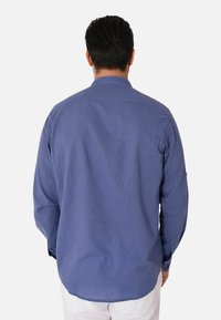 Camicia a maniche lunghe con bottoni in tessuto blu scuro uniforme, caratterizzata da un colletto classico e una vestibilità comoda. La vista posteriore mostra una texture liscia e cuciture.
