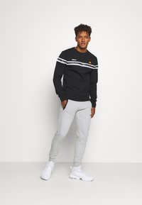 Black sweatshirt with white stripes across the chest, featuring a small logo. Paired with light gray joggers and white sneakers.