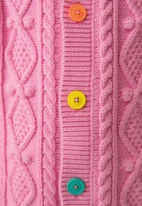 Ružový pletený kardigán s textúrovanými vzormi, ktorý má štyri farebné gombíky: oranžový, žltý, tyrkysový a zelený.