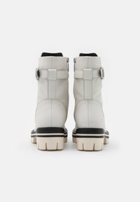 Botas de tobillo de cuero blanco con acentos negros, cuello acolchado y suela gruesa y estriada que presenta un borde claro contrastante.