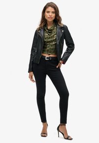 Zwarte leren motorjack gecombineerd met een groen met pailletten versierde top met een cowl-neck, zwarte skinny jeans en zwarte sleehakken met banden.