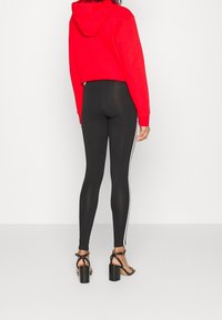 Svarta leggings med vita sidosträck, matchade med en röd kort hoodie. Svarta högklackade sandaler fulländar outfiten. Enkelt, avslappnat design.